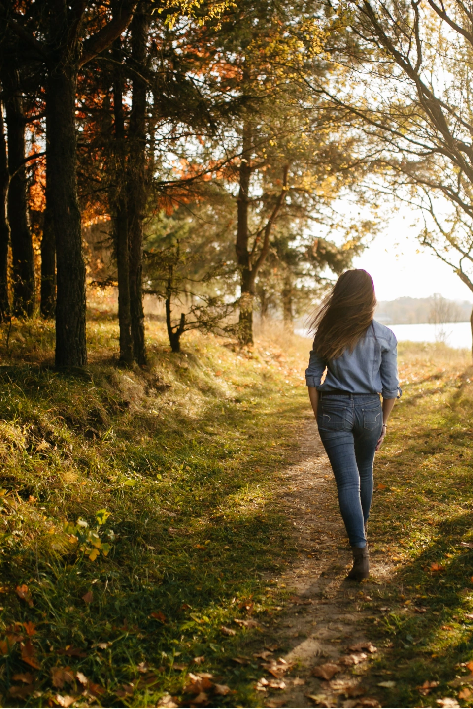 Woman walking along a tree-lined path in a park.